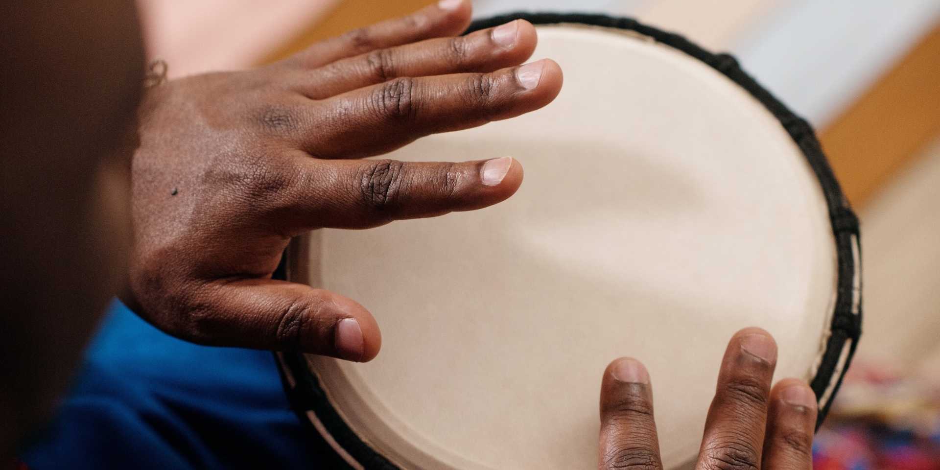 A man's hands hover over the skin of a djeme drum