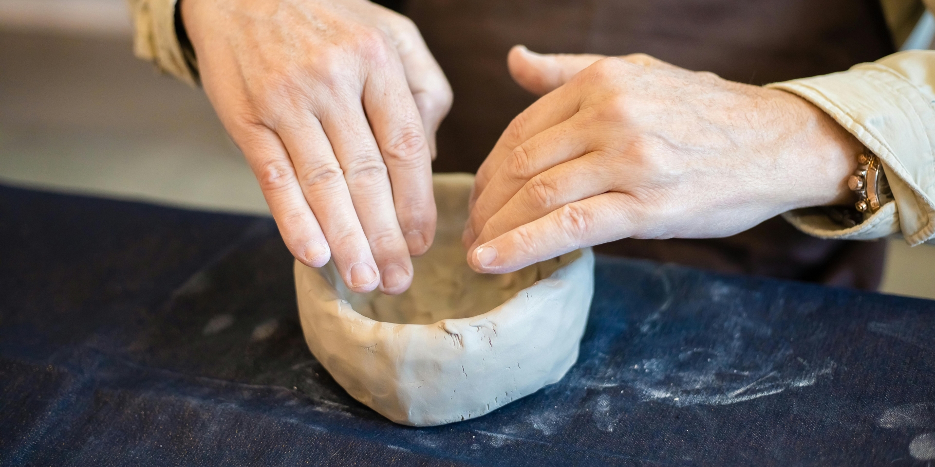 Hands pressing clay into the shape of a bowl