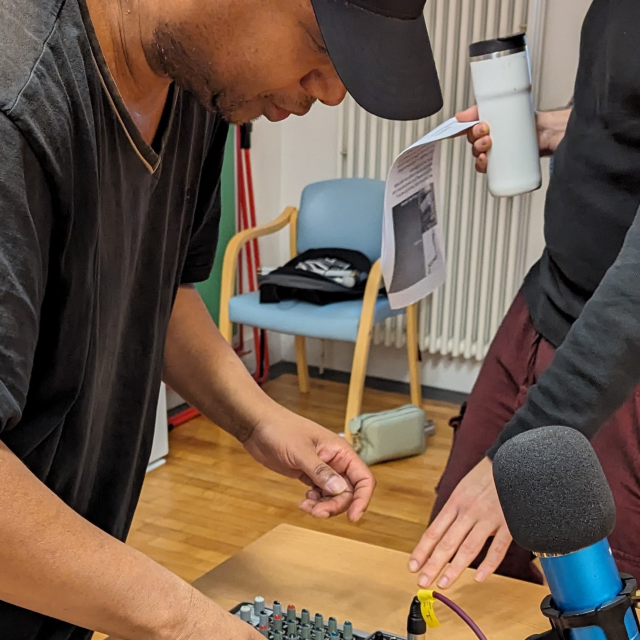 A man setting up to speak into the mic recording a Podcast with someone helping